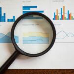 Magnifying glass over printed charts, comparing reports when choosing help desk software